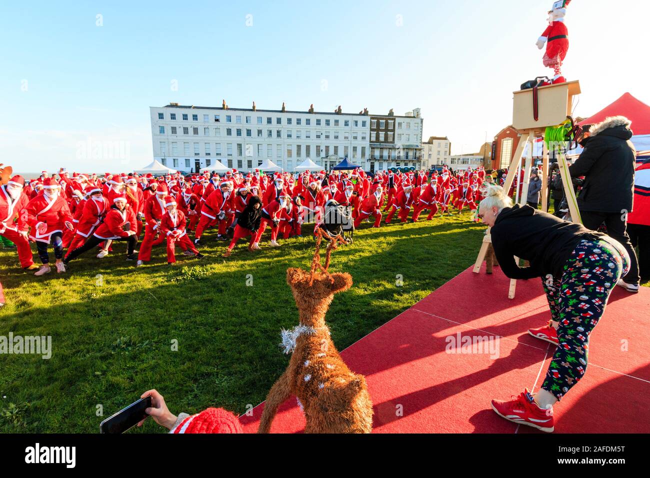 Eine große Gruppe von Menschen, die sich alle als Pater Xmas verkleidet haben, versammelte sich an der Küste von Margate für den jährlichen Pilgerhospiz-Spaßlauf "Santa am Strand". Gruppe, die während einer Gruppenübung den Anweisungen eines vor ihnen befindlichen Fitnesstrainers folgt. Stockfoto