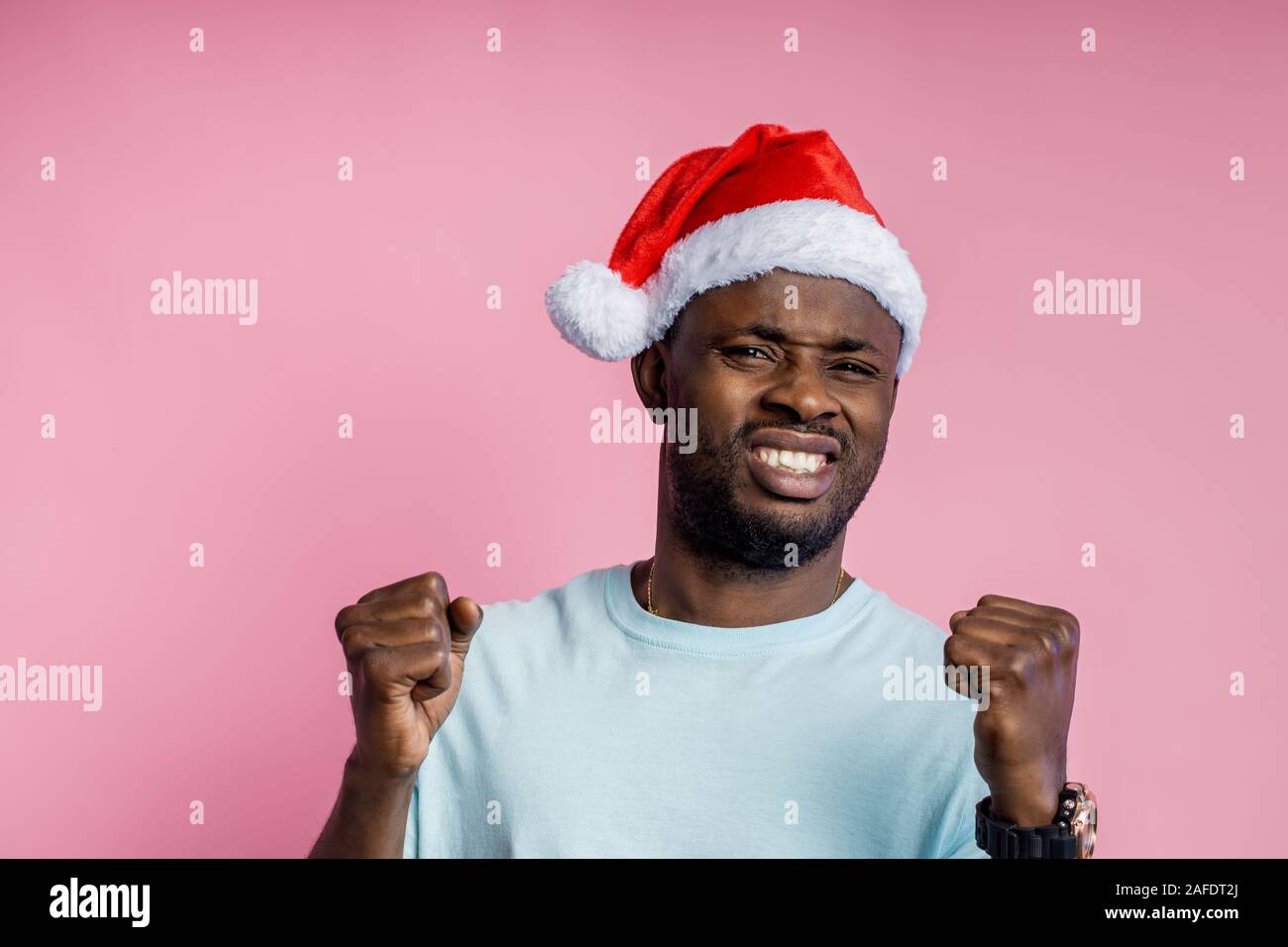 Frustriert, wütend, aggressiv afrikanischer Mann ballte die Fäuste und Zähne, Hände, tragen t-shirt, Santa hat, neben der Suche mit wütenden Ausdruck, p Stockfoto
