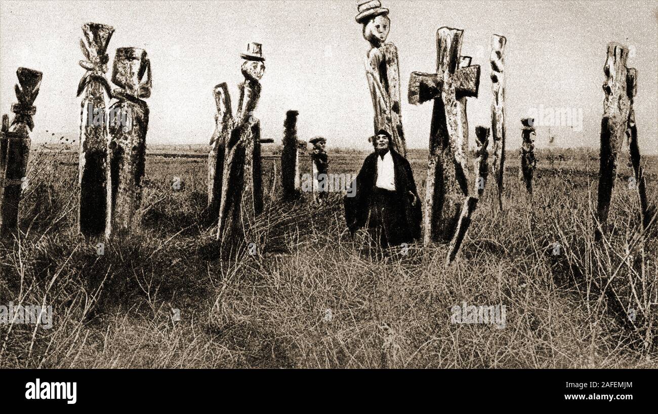 Eine 1920 Foto von araucanian Indian Grab marker Totempfähle im chilenischen Patagonien mit einem merkwürdigen Dracula - wie Besucher, wahrscheinlich einen Eingeborenen Mapuche Das wird durch (Chief) ot Toki (Ax Inhaber) Indische tragen einen Mantel. Mapuche wurden seit Generationen für die Textilien von Frauen gewebt bekannt Stockfoto