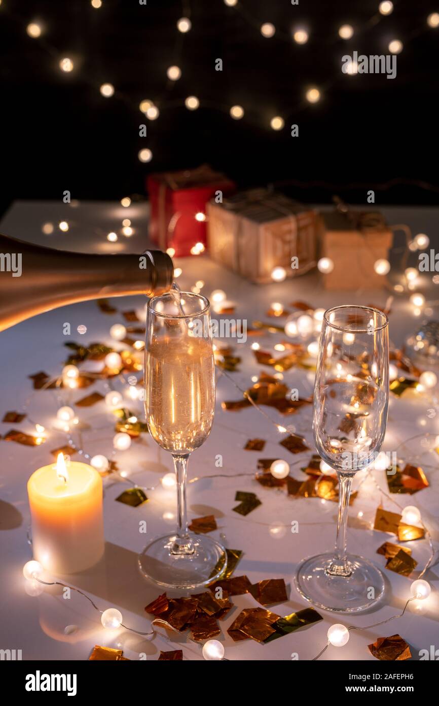 Zwei Flöten und brennende Kerze auf dem Tisch unter den goldenen Girlanden Konfetti und Lit Stockfoto