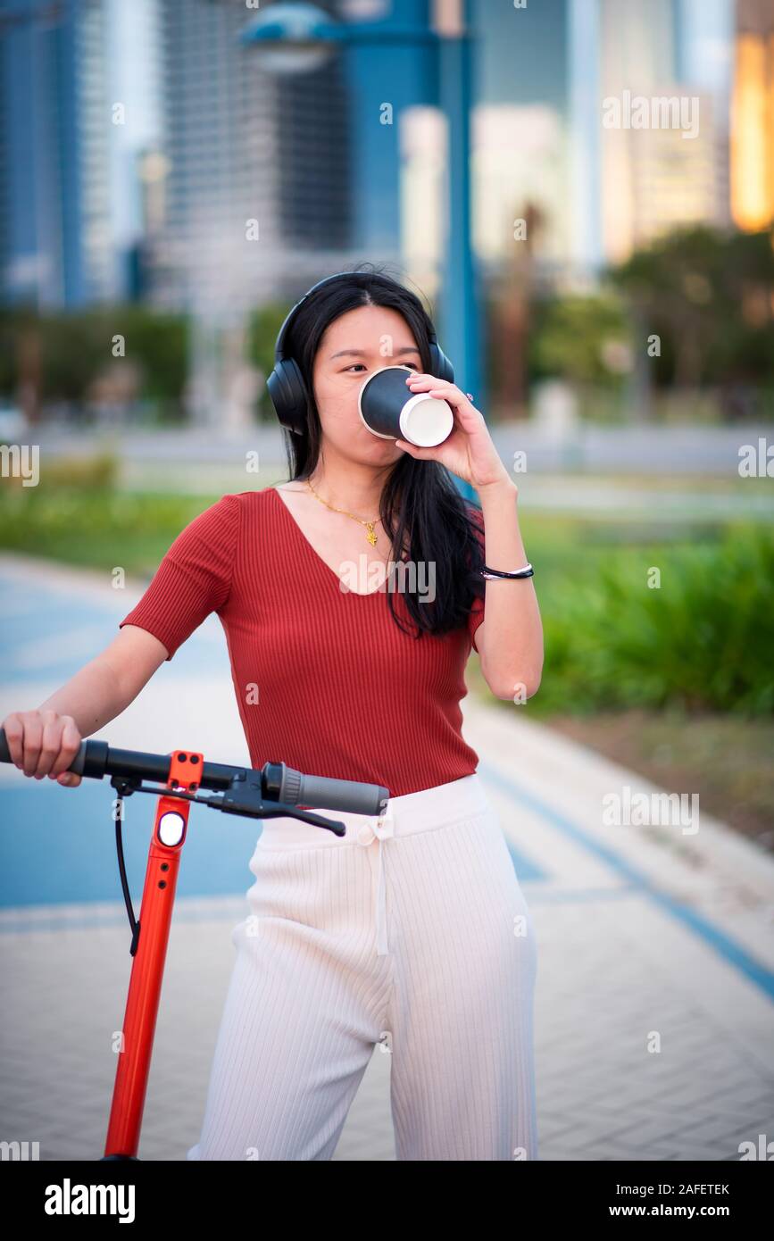 Frau mit einem Kaffee Bremse bei der Verwendung von elektrischen scooter in einer modernen Stadt Stockfoto