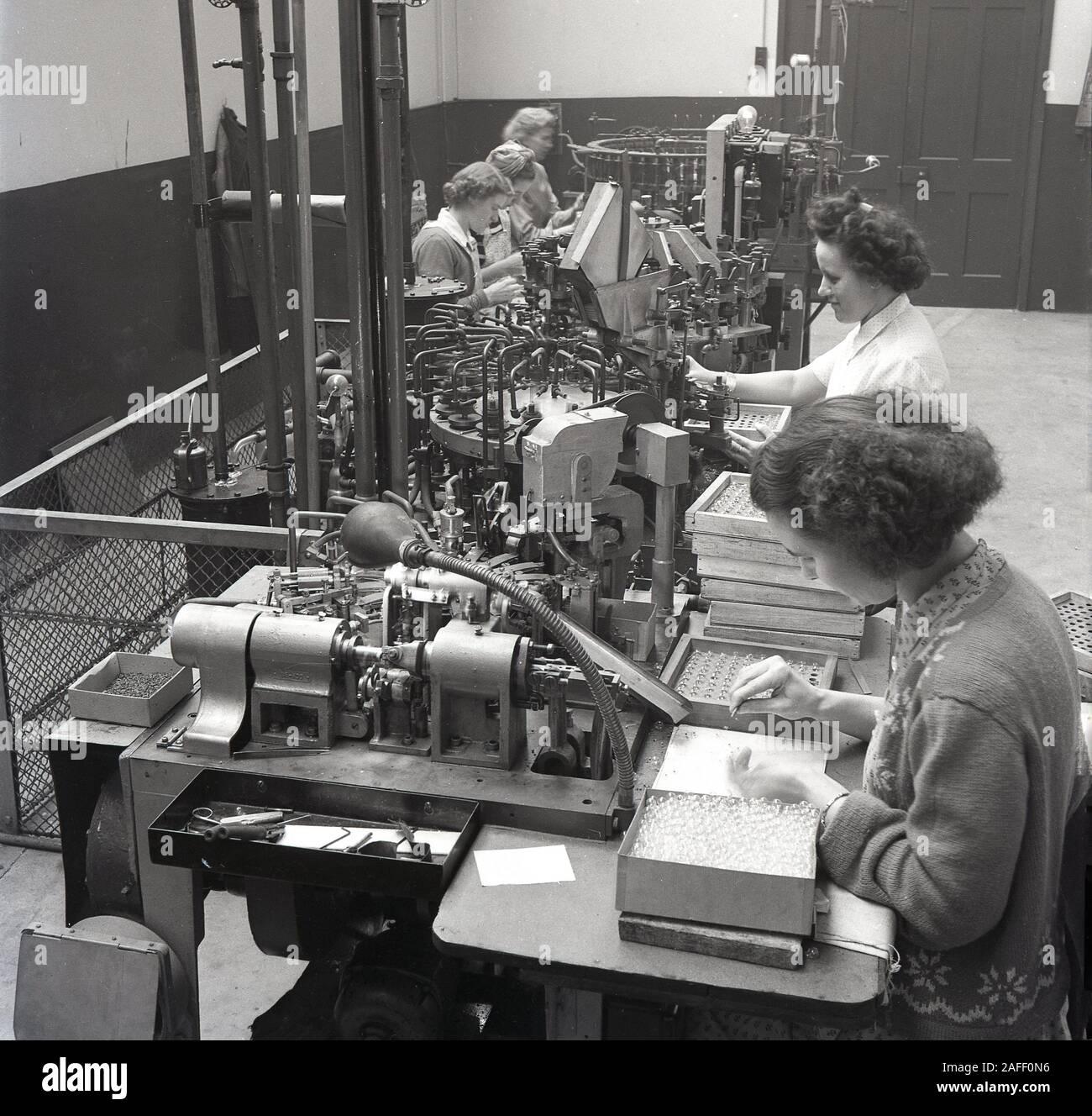 1950er Jahre, historische, weibliche Fabrikarbeiter, die Maschinen der damaligen Zeit bei der Herstellung von Glühbirnen verwendeten, England, Großbritannien. Stockfoto