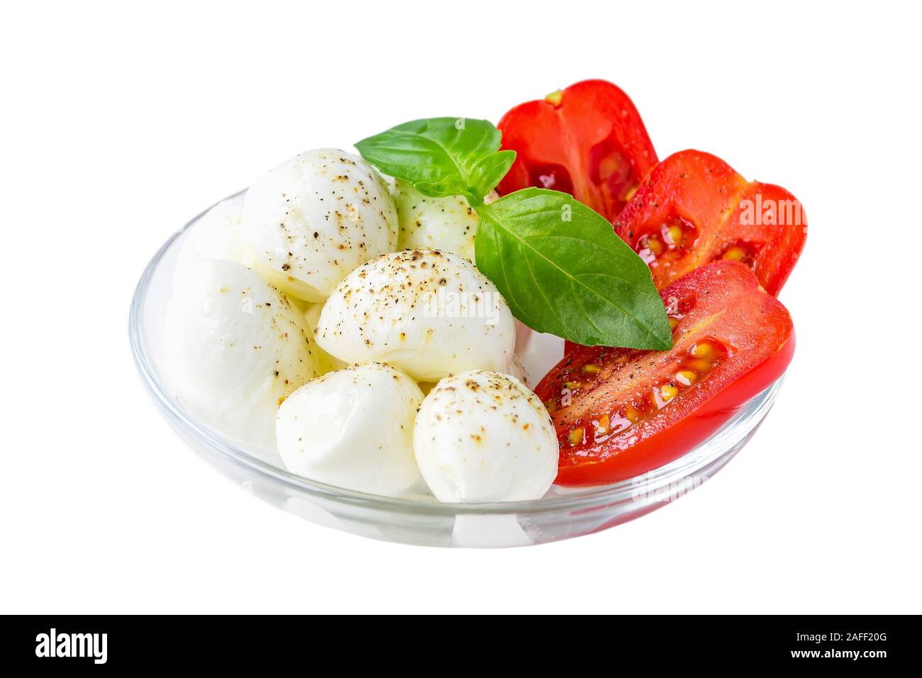 Caprese Salat auf weißem Hintergrund. Mini Kugeln Mozzarella mit Basilikum und rote Kirschtomaten in einer Glasschale. Mediterrane Küche. Stockfoto