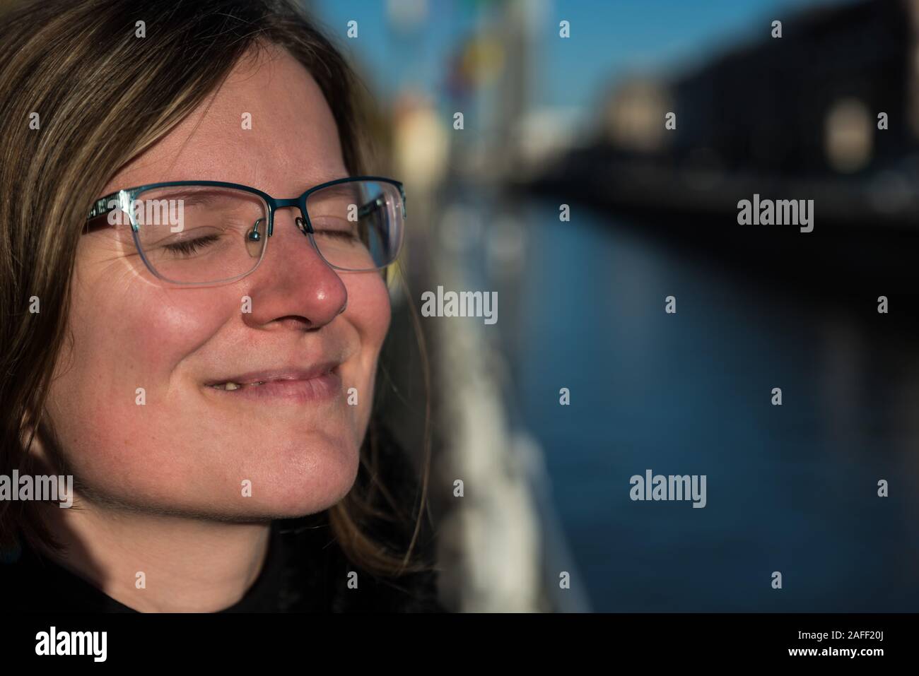 Die dreißigjährige attraktive Frau posiert am Brüsseler Kanal in der Sonne, die Augen sind geschlossen Stockfoto