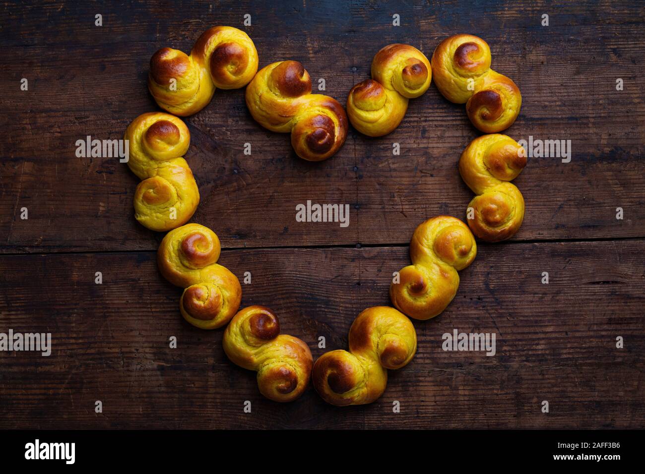 Schwedische traditionelle Weihnachten bun Lussekatter oder Lussebullar auf einem rustikalen Holztisch, in der Form eines Herzens. Die Brötchen sind frisch und hausgemacht Stockfoto