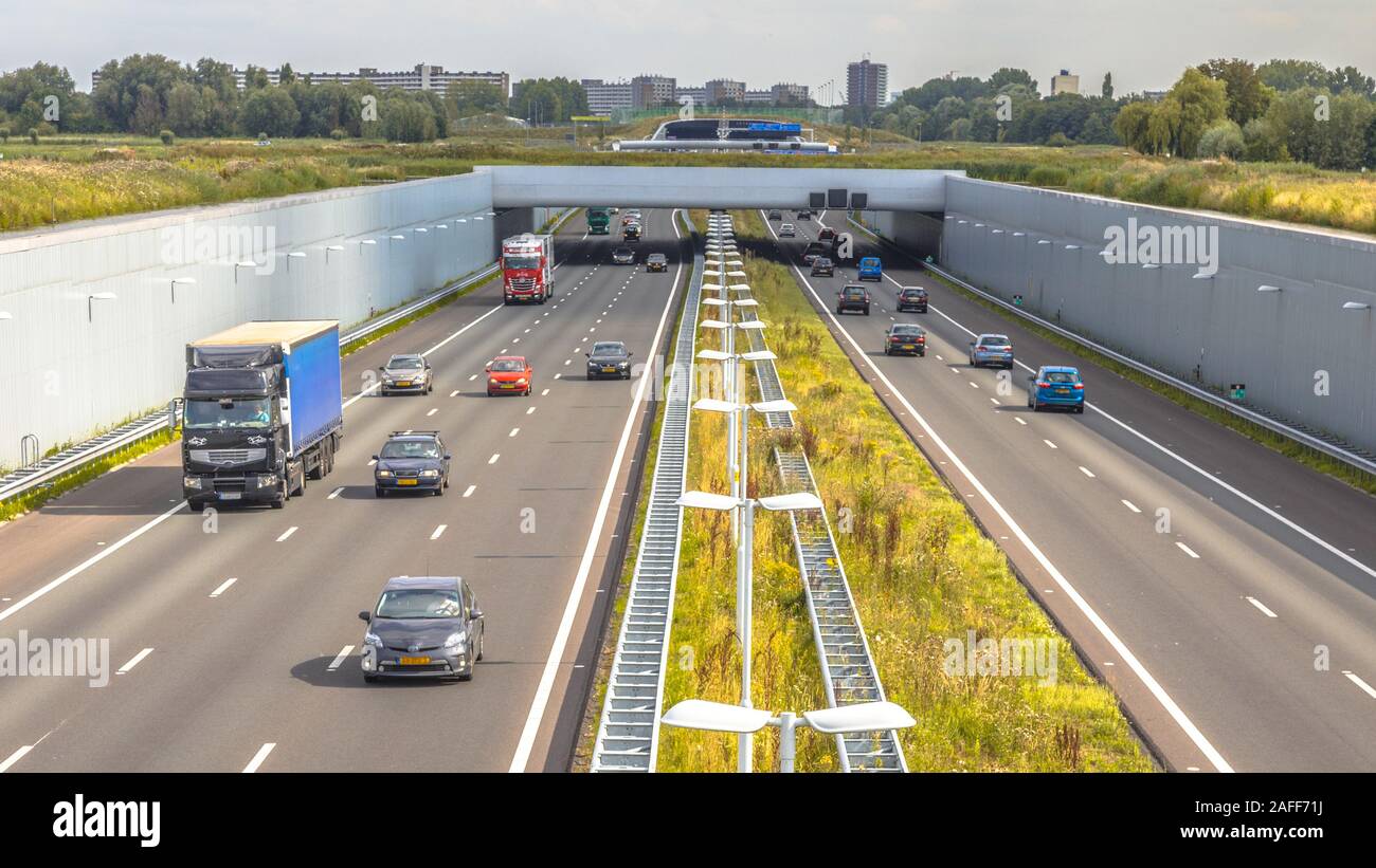 Das Pendeln der Verkehr auf der Autobahn a4 in der Nähe von Den Haag Gegend Randstad. Autobahn Kreuzung aquaduct Tunnel mit städtischen Gebiet von Rotterdam im Hintergrund, Niederlande. Stockfoto