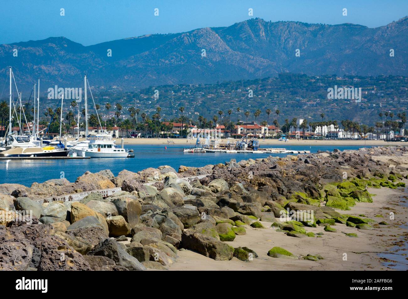 Eine weitläufige Aussicht auf den Hafen von Santa Barbara mit angedockten Segelboote und felsigen Wellenbrecher mit grünen Algen mit Santa Ynez Mountains, Santa Barbara, CA Stockfoto