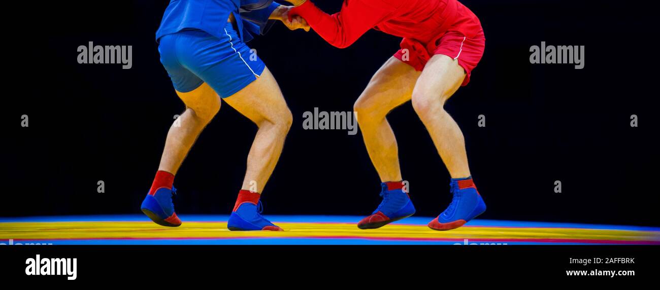 Zwei Männer in blauen und roten Sambo wrestling auf einem gelben wrestling Teppich in der Turnhalle Stockfoto