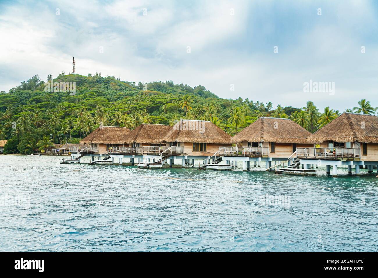 Blick auf eine Reihe von typischen strohgedeckten Beachside Überwasser Bungalows durch einen von Palmen gesäumten Strand auf Bora Bora, einer kleinen Insel im Südpazifik in Französisch-Polynesien Stockfoto