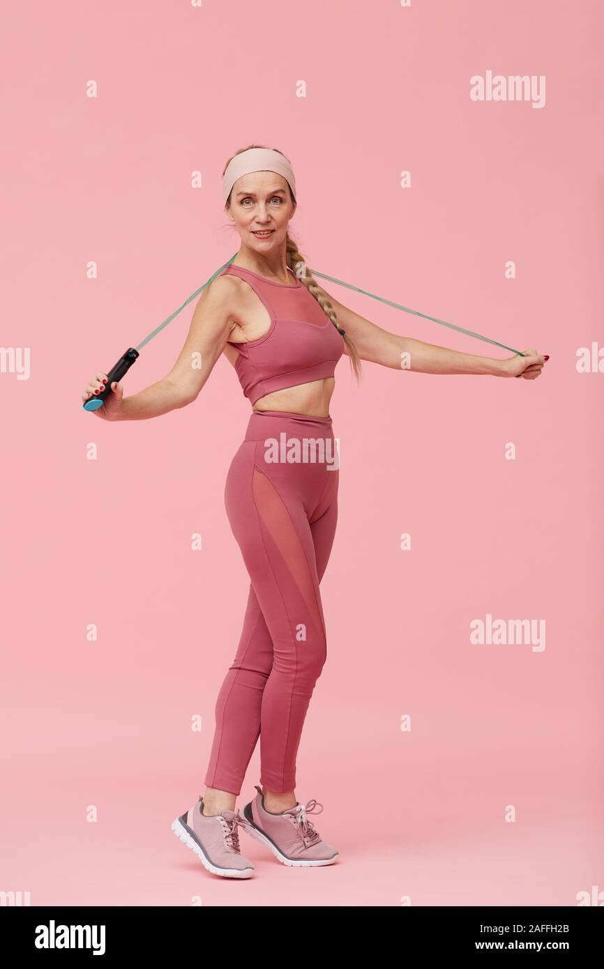 In voller Länge Porträt der Schönen reife Frau tragen Sport Outfit mit Seilspringen gegen Pastell rosa Hintergrund posiert Stockfoto