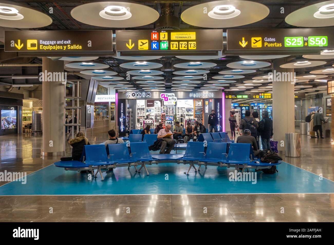 Die Leute sitzen auf den Sitzen in der Abfahrt am Terminal 4 S von Adolfo Suárez Flughafen Barajas in Madrid, Spanien. Stockfoto