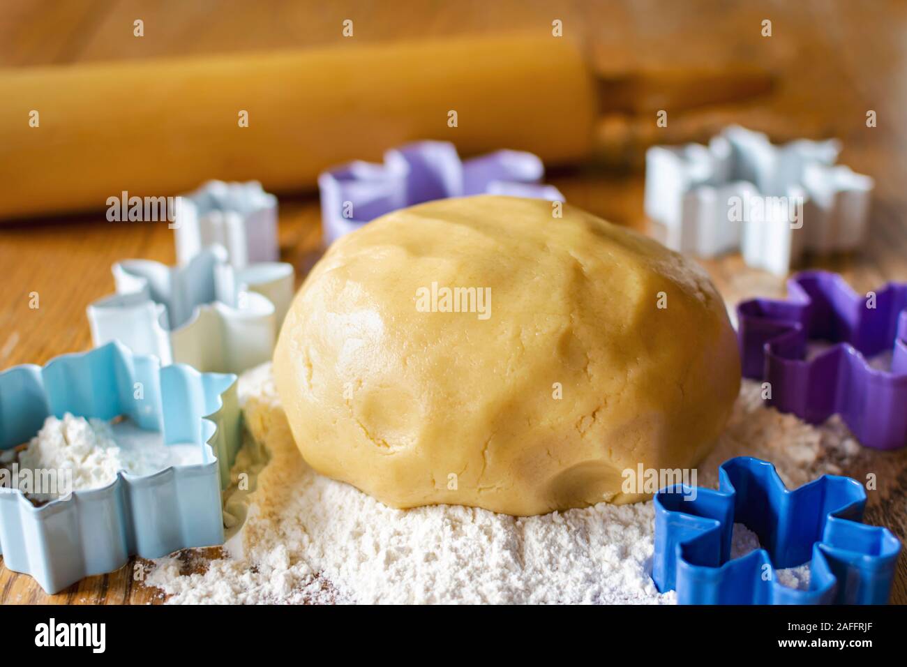 Eine Kugel von Zucker Plätzchenteig in einem Bett von Mehl. Rolling Pin unscharf im Hintergrund. Verschiedene Blumen- und Schneeflocke Ausstecher rund um Ball von Teig Stockfoto