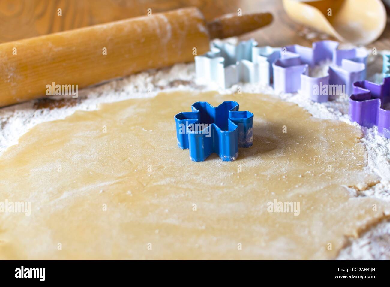 Blaue Blume Cookie Cutter Ein ausgerollt Zucker Plätzchenteig. Zusätzliche Schneeflocke und Blume Ausstecher unscharf im Hintergrund. Holz- Rollen Stockfoto