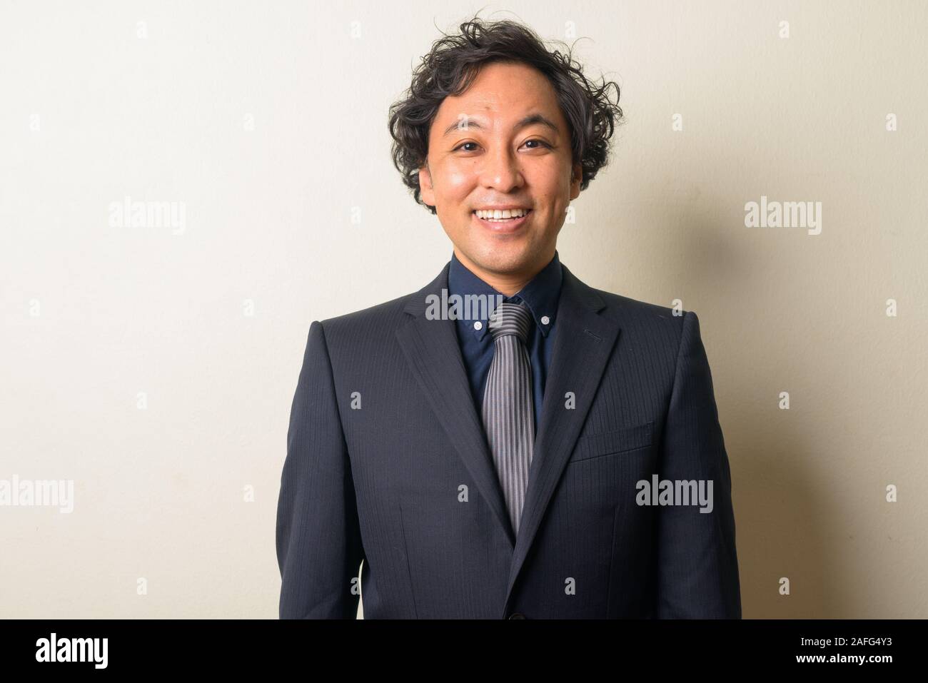 Angesichts der glückliche Japanische Geschäftsmann in Anzug mit lockigem Haar lächelnd Stockfoto