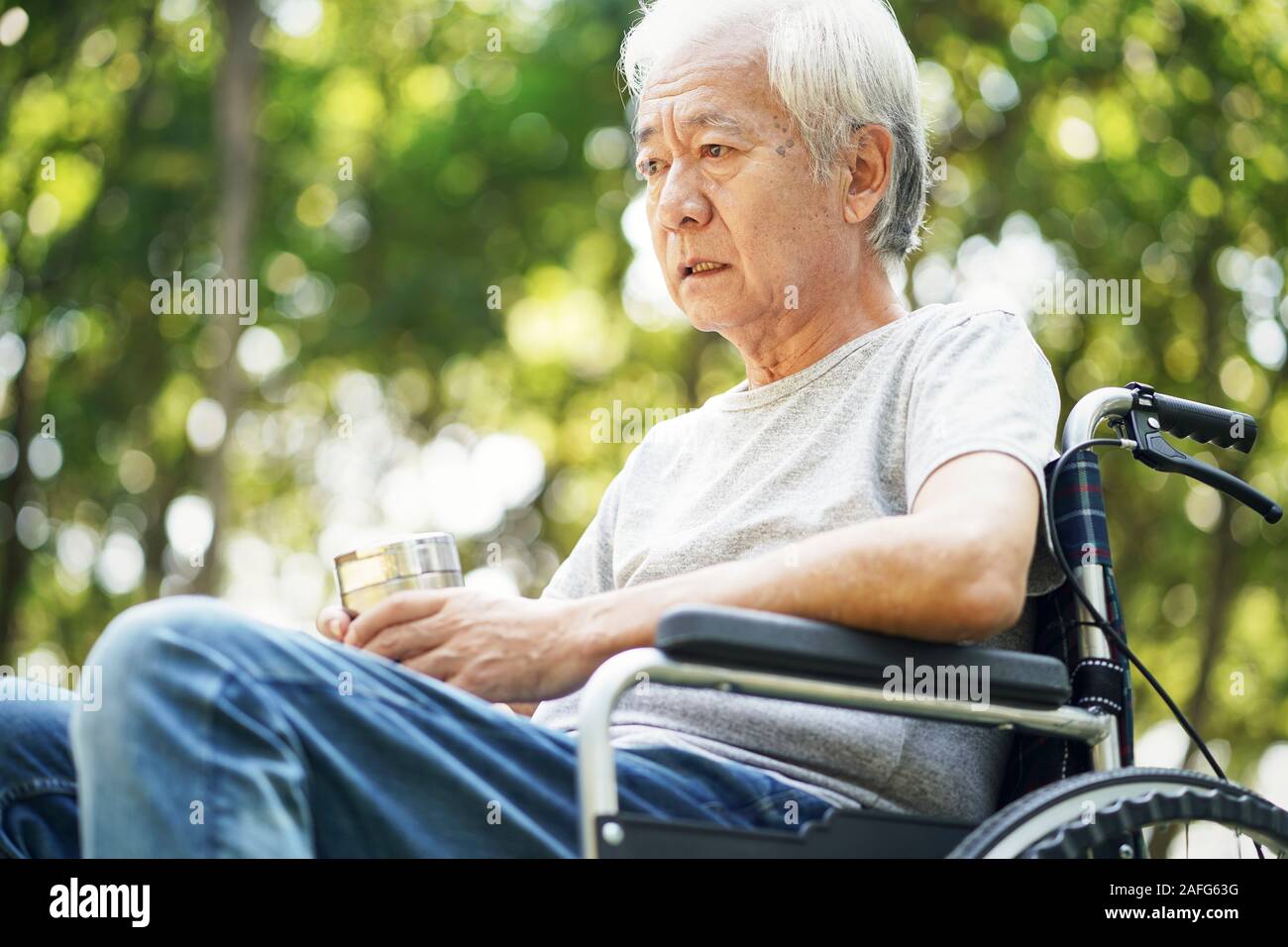 Traurig asiatischen älterer Mann sitzt draußen im Rollstuhl Stockfoto