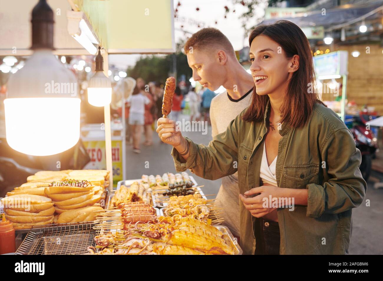 Glückliche junge Frau kaufen Schweinefleisch vom Grill Spieß mit traditionellen vietnamesischen Street Food stall Stockfoto