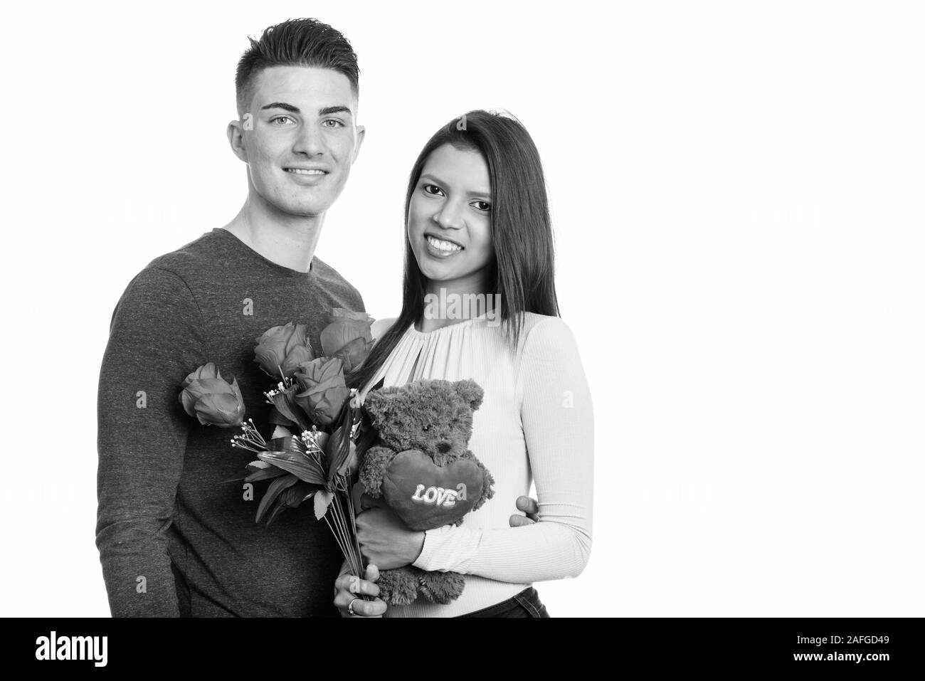 Junge glückliches Paar lächelnd, während sie rote Rosen und Teddybär mit Herz und Liebe Zeichen Stockfoto