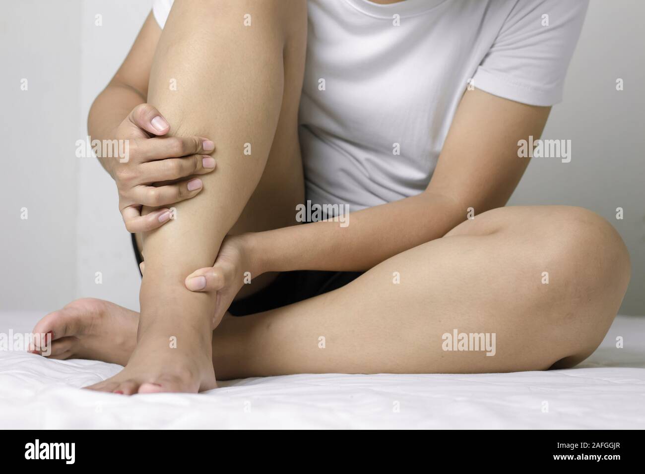 Frau massieren Ihren Knöchel, weil der Schmerz. Schmerzen im Knöchel im Konzept der Gesundheit. Sitzung squeeze Knöchel auf dem weißen Bett. Stockfoto