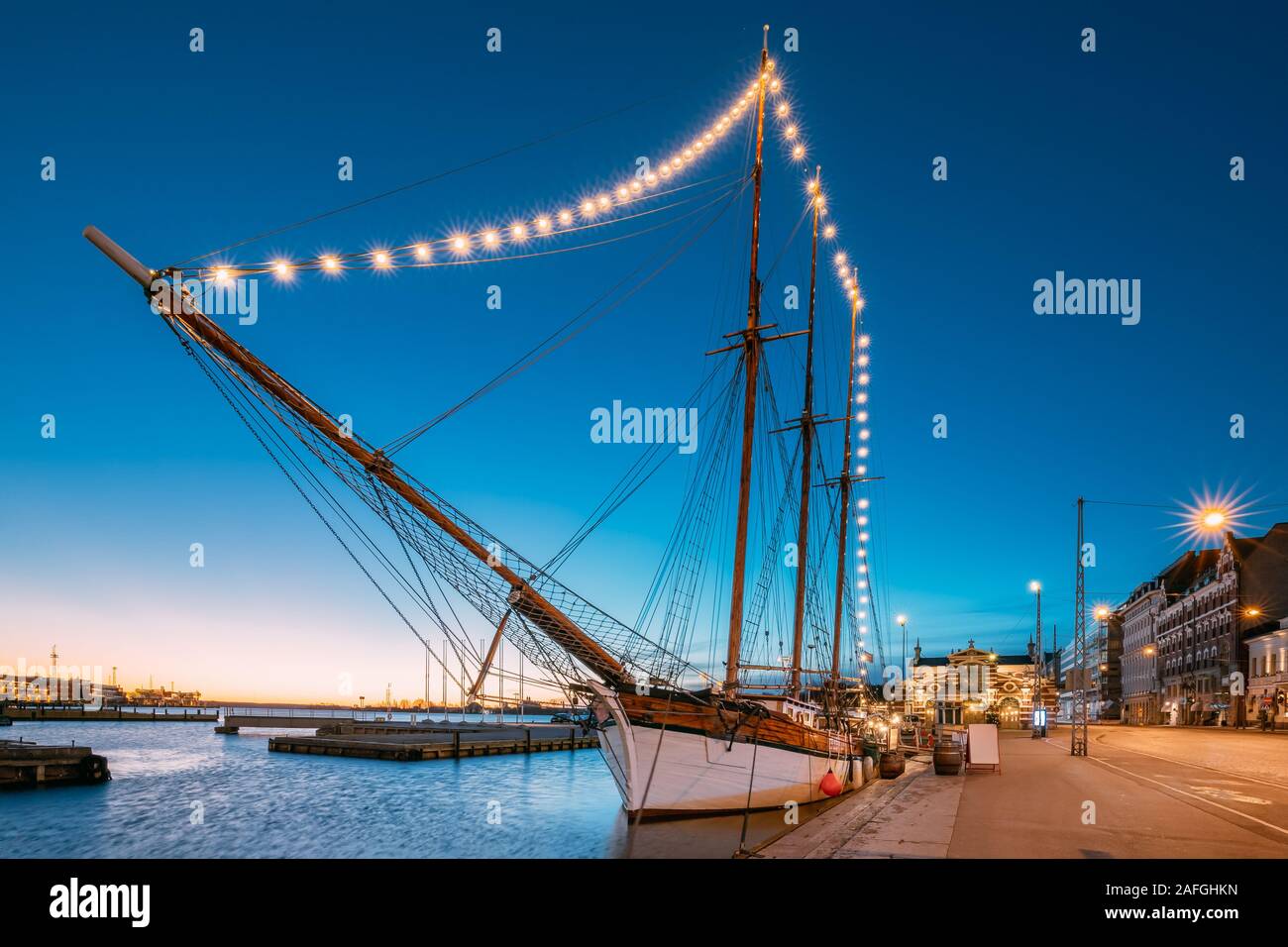 Helsinki, Finnland. Alte hölzerne Segelboot Schiff Schoner ist mit der Stadt Pier, Steg vertäut. Ungewöhnliche Cafe Restaurant im Stadtzentrum in Beleuchtung in Ev Stockfoto