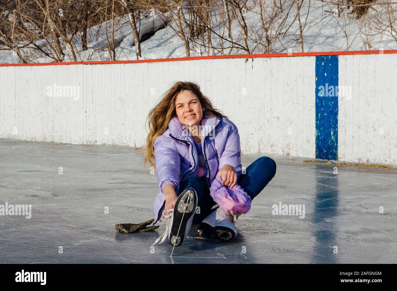 Reizende junge Frau sitzt auf der Eisbahn und tieing Schnürsenkel Stockfoto