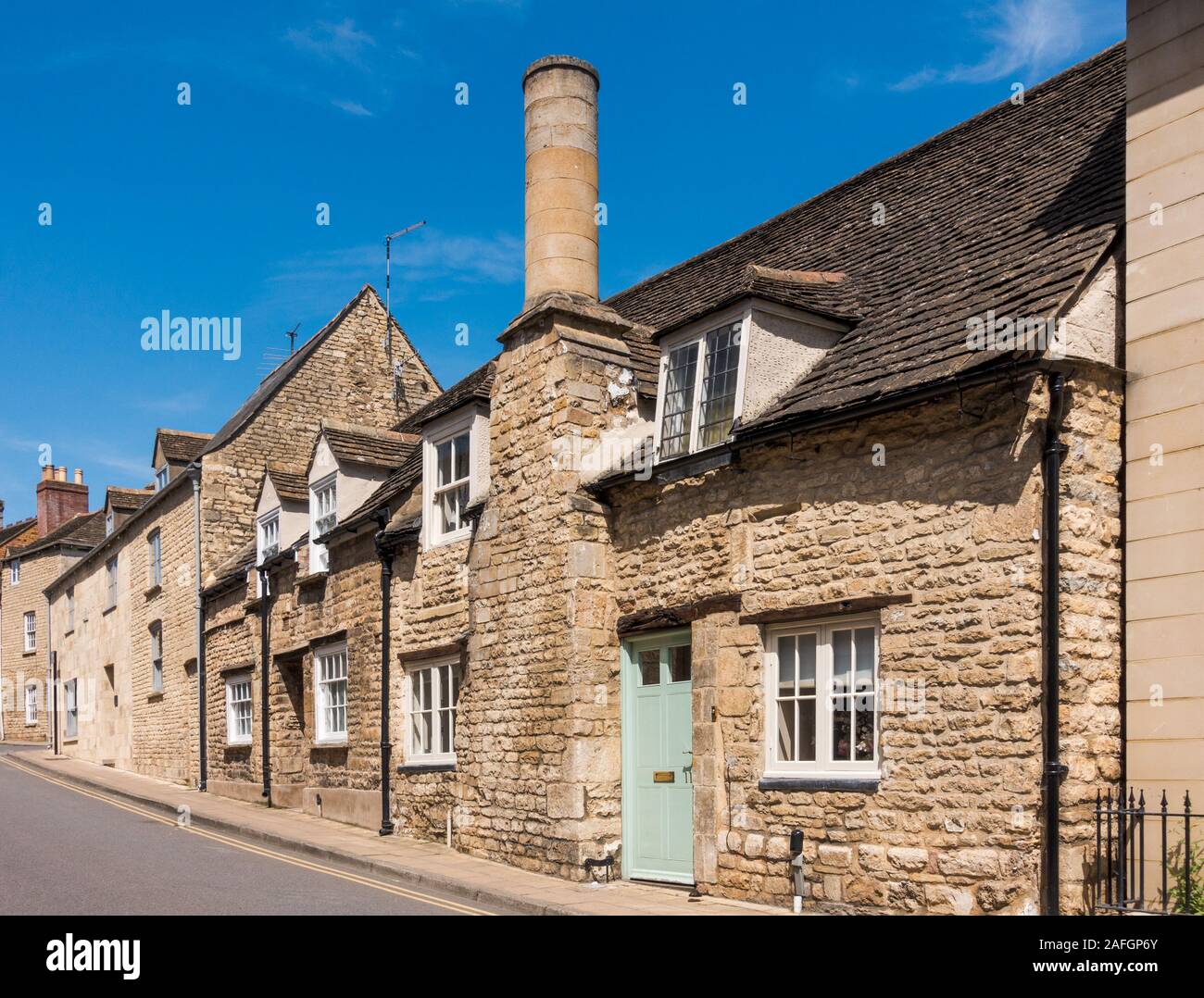 Eine Reihe sonnenbeleuchteter, denkmalgeschützter kleiner Steinhäuser, eines mit einem großen kreisförmigen Steinkamin, St. George's Street, Stamford, Lincolnshire, England, Großbritannien Stockfoto