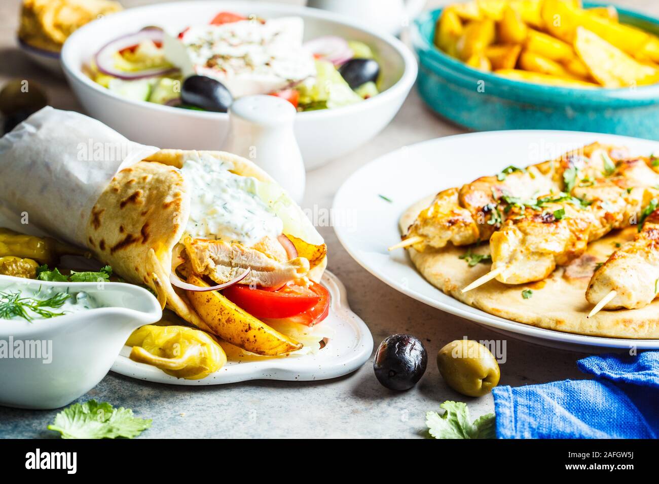 Griechisches Essen: Salat, Hähnchen Souvlaki, Gyros und gebackene Kartoffeln auf einem grauen Hintergrund. Traditionelle griechische Küche Konzept. Stockfoto