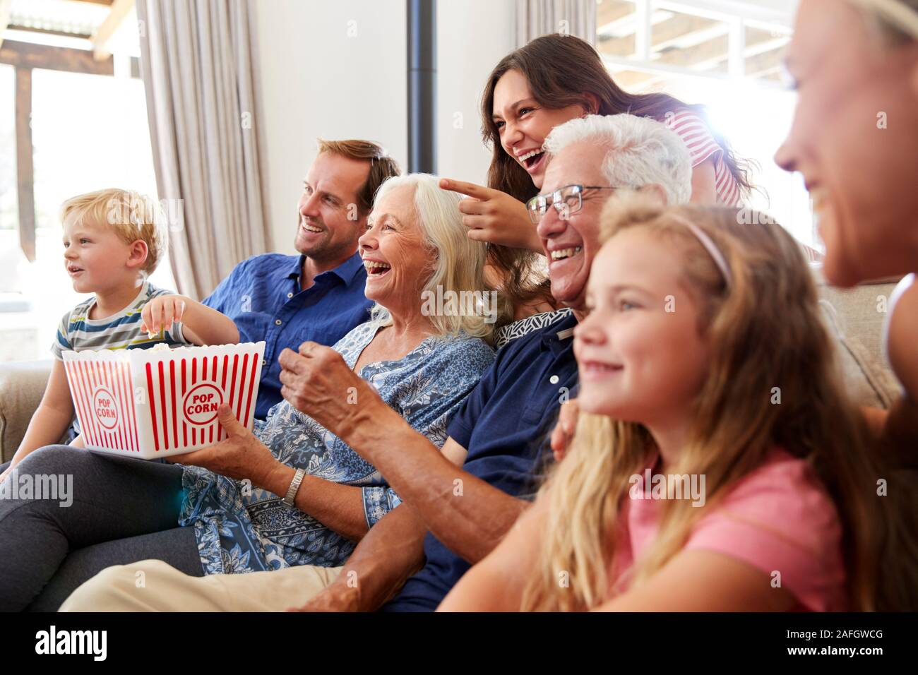 Multi-Generation Familie sitzt auf dem Sofa zu Hause essen Popcorn und Film zusammen Stockfoto