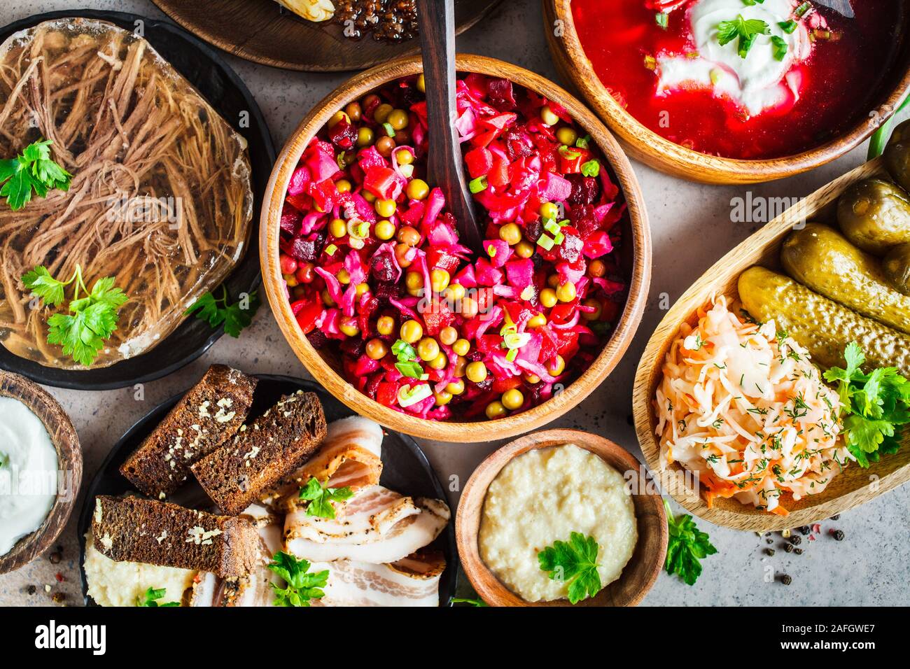 Traditionelle russische Küche Konzept. Borsch, sülze Fleisch, Speck, Pfannkuchen, Salat Vinaigrette und Sauerkraut, grauen Hintergrund. Stockfoto