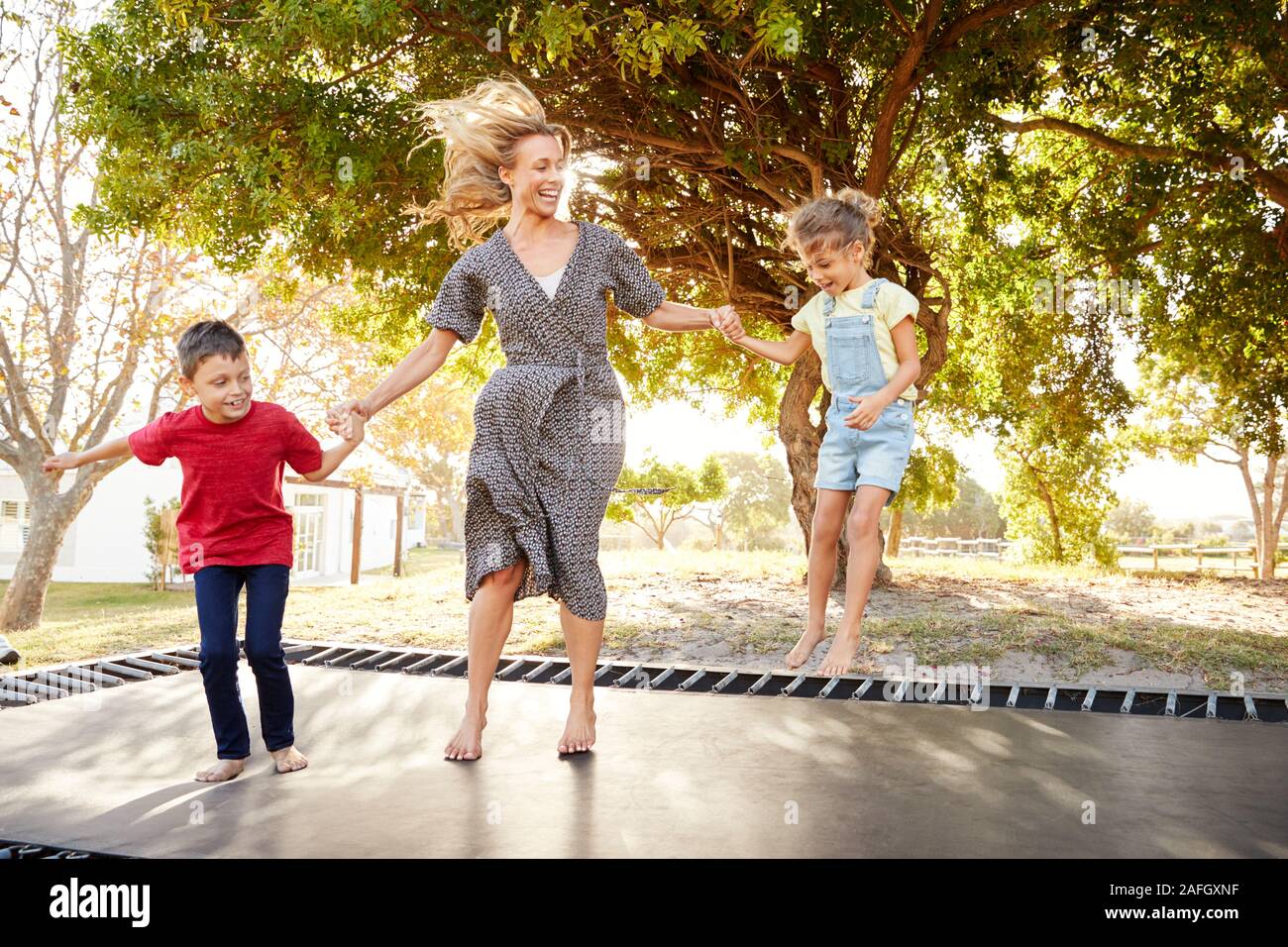 Mutter spielt mit Kindern auf Outdoor Trampolin im Garten Stockfoto