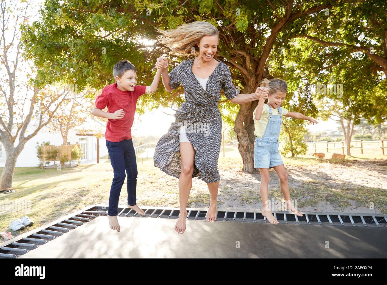 Mutter spielt mit Kindern auf Outdoor Trampolin im Garten Stockfoto