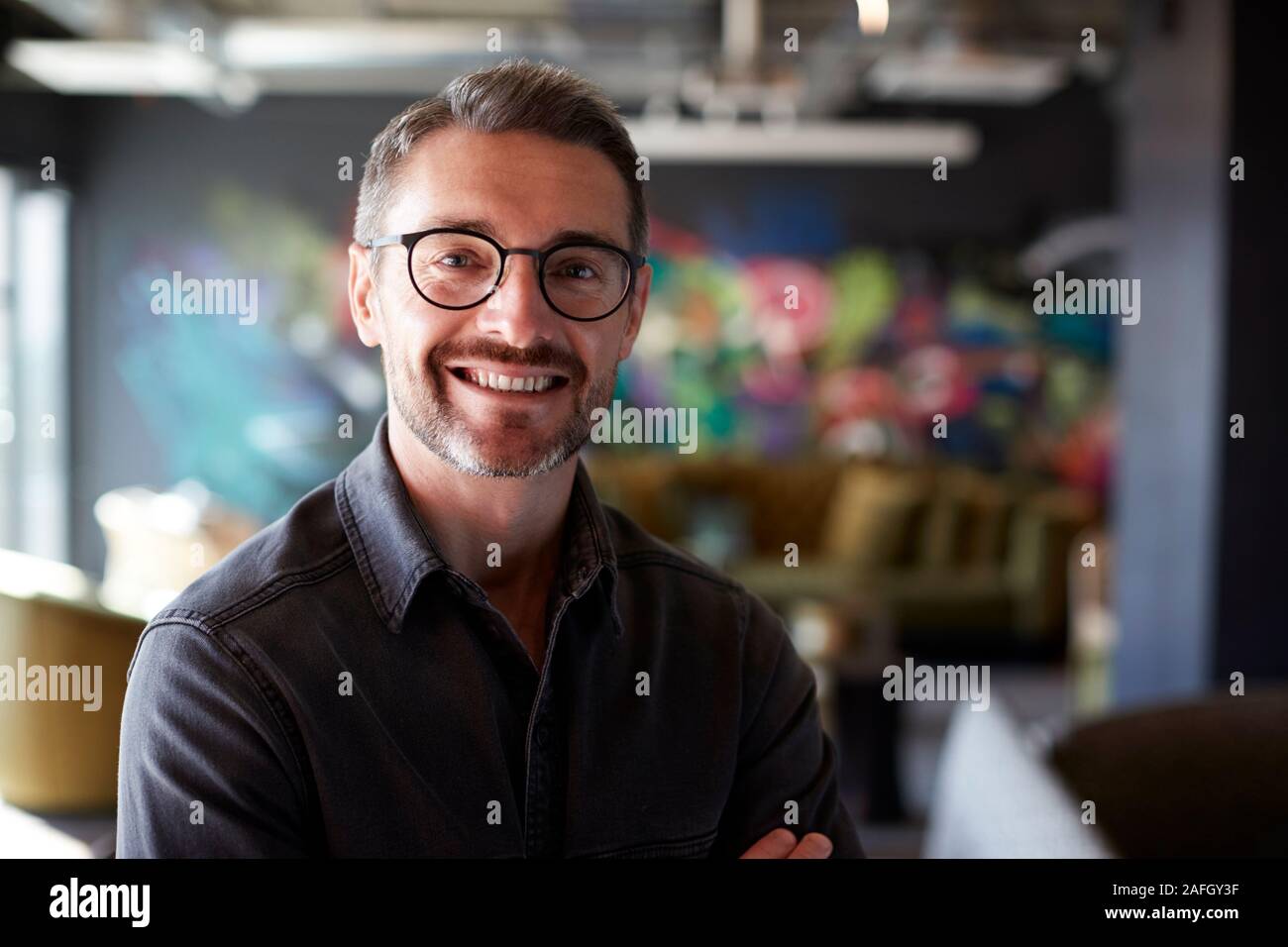 Weißer Mann mittleren Alters kreativ in der beiläufigen office Lounge blickt in die Kamera lächeln, Nahaufnahme Stockfoto