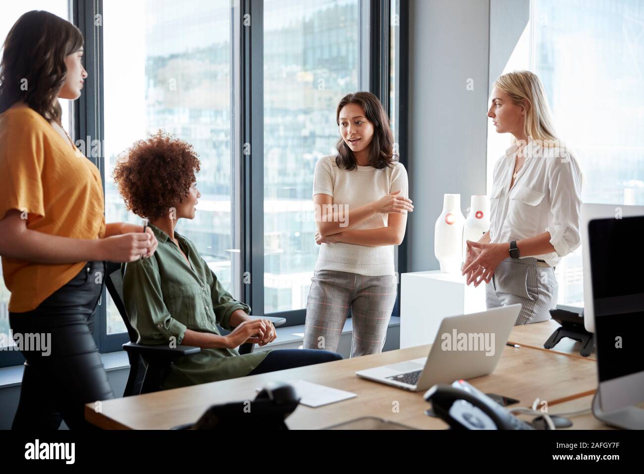 Vier weibliche Kollegen in der Diskussion an einem Schreibtisch in einem kreativen Büro, drei Viertel Länge Stockfoto