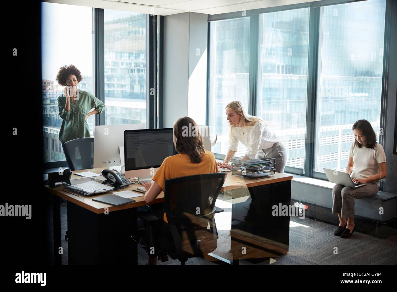 Vier weibliche kreative Kollegen zusammen die Arbeit in einem Büro, durch Glas mit Reflexion gesehen Stockfoto