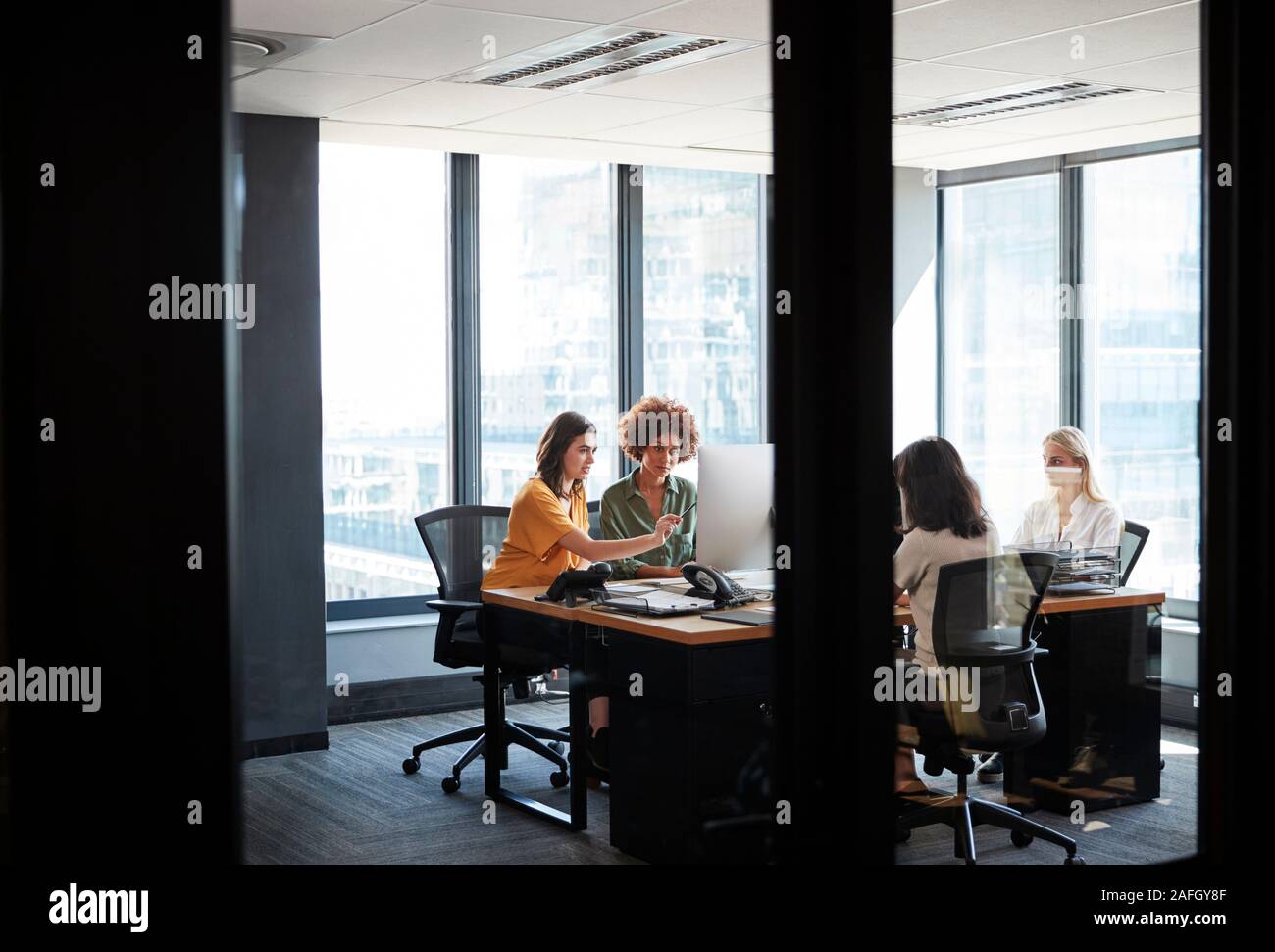 Vier weibliche kreative Kollegen beschäftigt, die Arbeit in einem Büro, durch eine Glaswand mit Text auf es gesehen Stockfoto