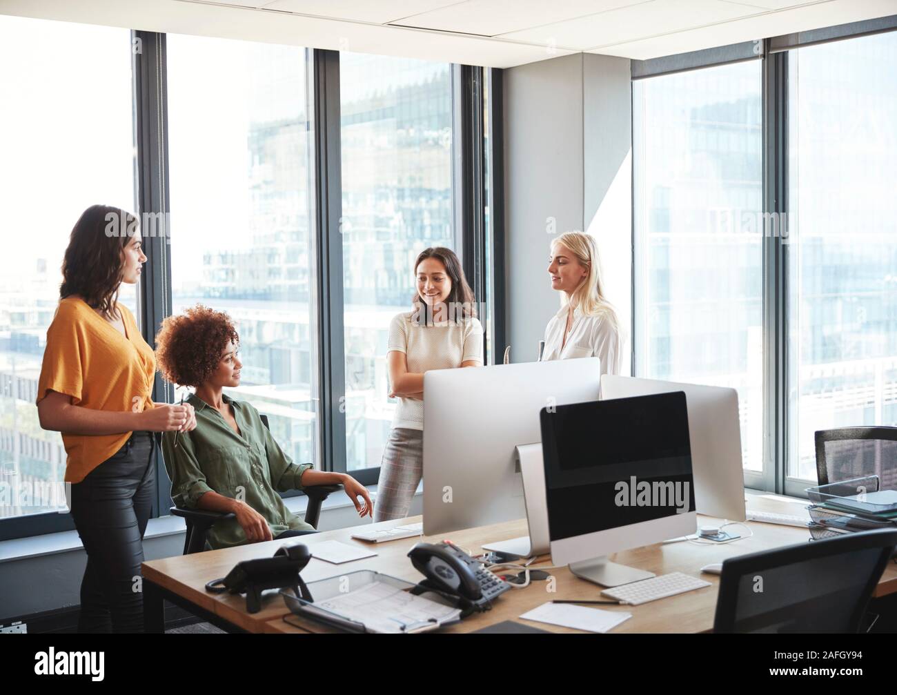 Vier weibliche Kollegen in der Diskussion an einem Schreibtisch in einem kreativen Büro, zu jeder anderen Suchen Stockfoto