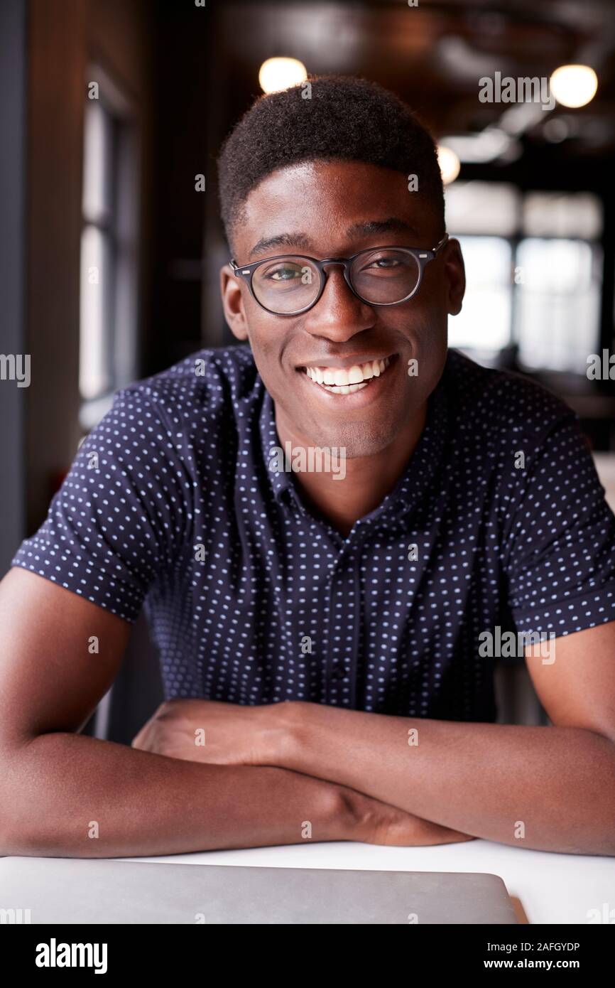 Tausendjährige männlichen Schwarzen kreative Sitzen an einem Schreibtisch in einem Büro lächelnd in die Kamera, Nahaufnahme, vertikal Stockfoto