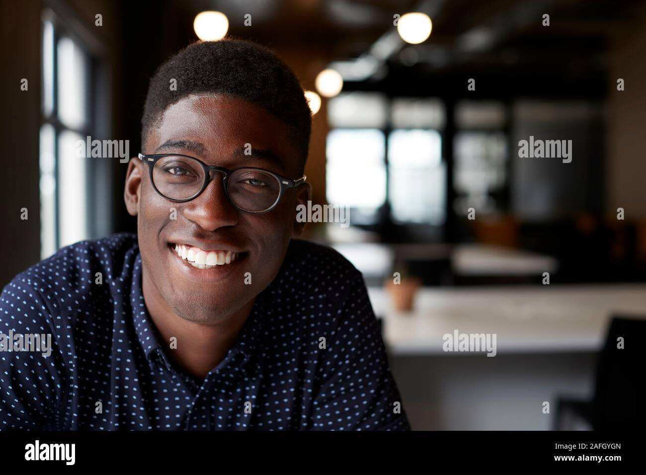 Tausendjährige männlichen Schwarzen kreative Sitzen an einem Schreibtisch in einem Büro lächelnd in die Kamera, in der Nähe Stockfoto