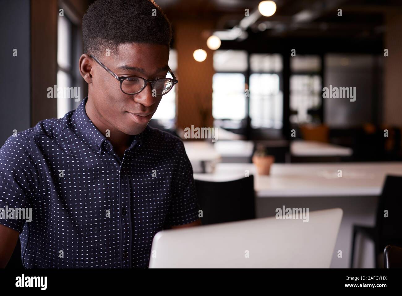 Junge schwarze Männer kreative Sitzen an einem Schreibtisch in einem offenen mit Laptop plan Office, Nahaufnahme, Seitenansicht Stockfoto