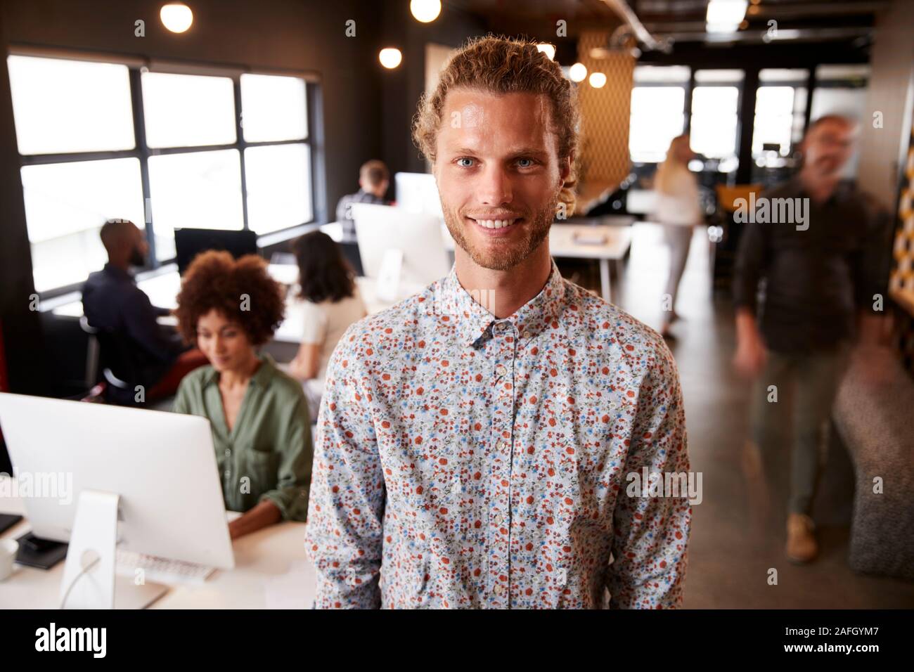 Tausendjährige weißen männlichen Kreative stehen in einem langen gemütlichen Büro, Lächeln für die Kamera Stockfoto