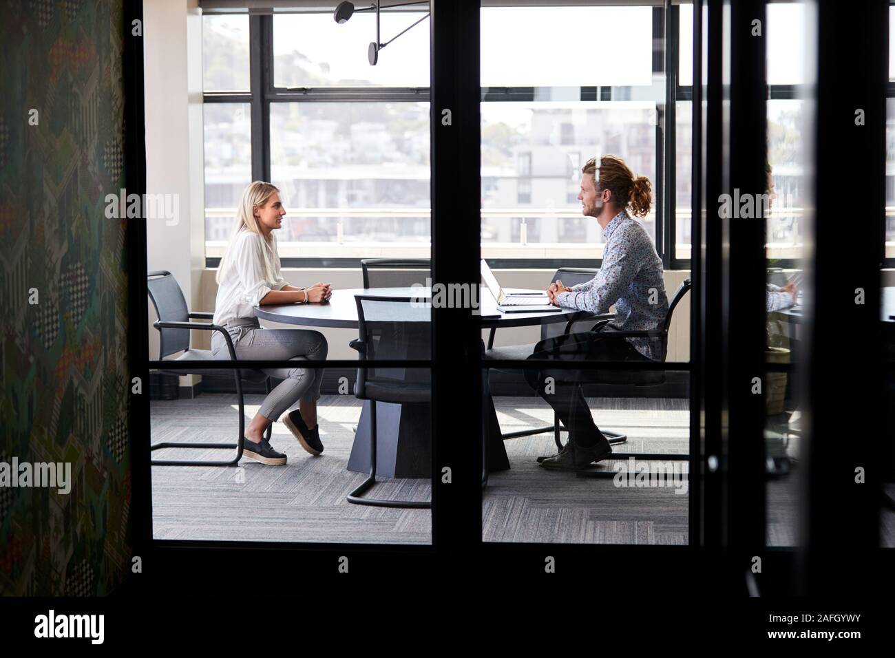 Zwei tausendjährige business Creatives in einem Konferenzraum für ein Vorstellungsgespräch, durch Glaswand gesehen Stockfoto