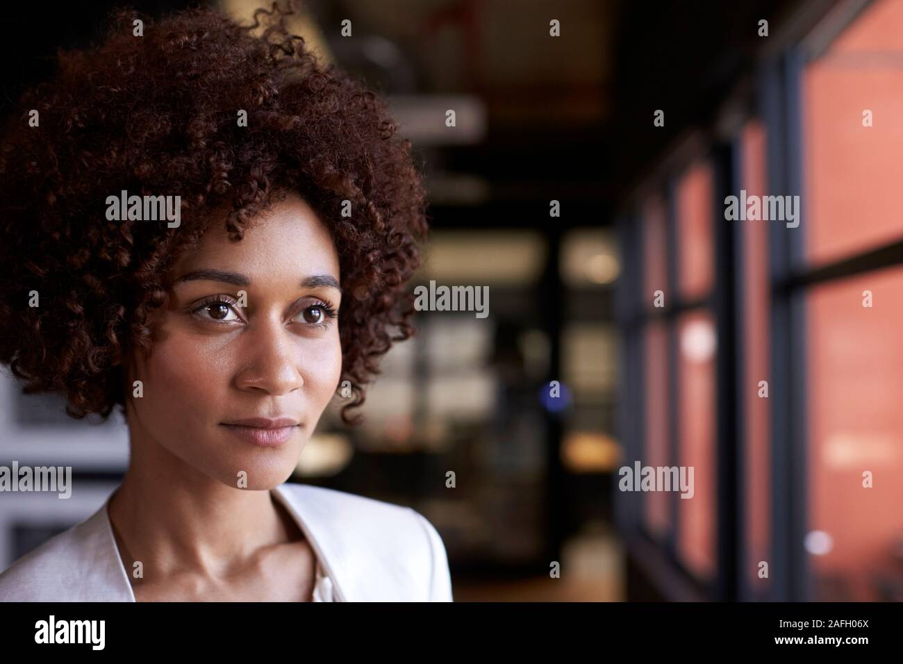 Tausendjährige schwarz Geschäftsfrau, schauen aus dem Fenster in einem Büro, Kopf und Schultern, in der Nähe Stockfoto