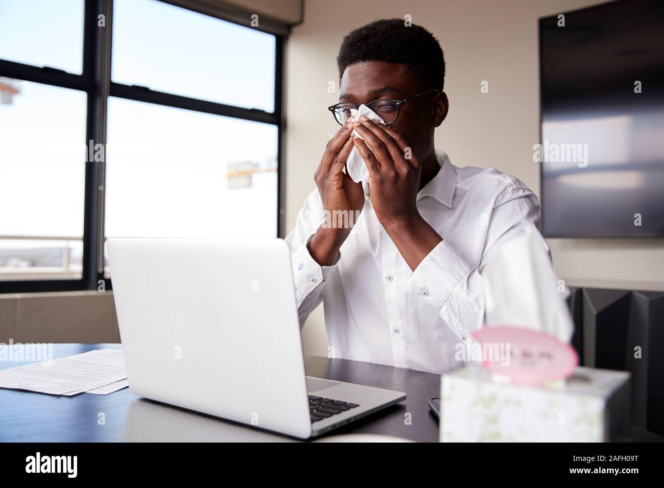 Junge schwarze Unternehmer im Büro seine Nase in ein Gewebe sitzen Stockfoto
