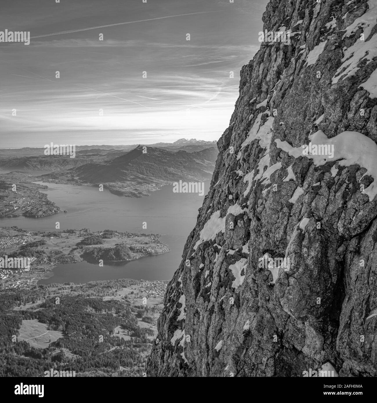 Graustufen Nahaufnahme von Felsen mit Wäldern und einem See umgeben Durch felsige Berge im Hintergrund Stockfoto