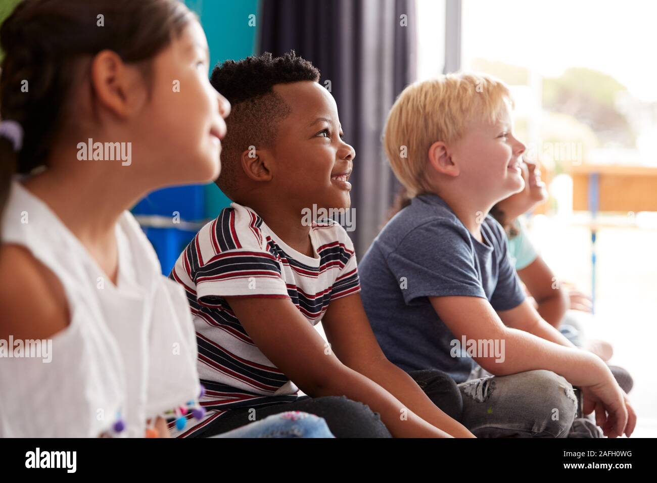 Gruppe von Grundschülern sitzen auf dem Boden hören Lehrer Stockfoto