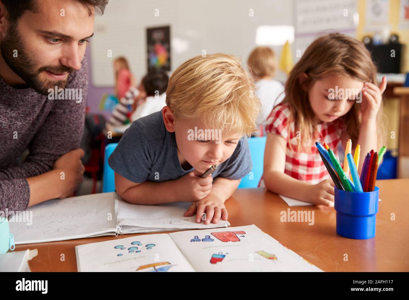 Grundschule Lehrer helfen Schülerinnen und Schüler bei der Arbeit am Schreibtisch im Klassenzimmer Stockfoto