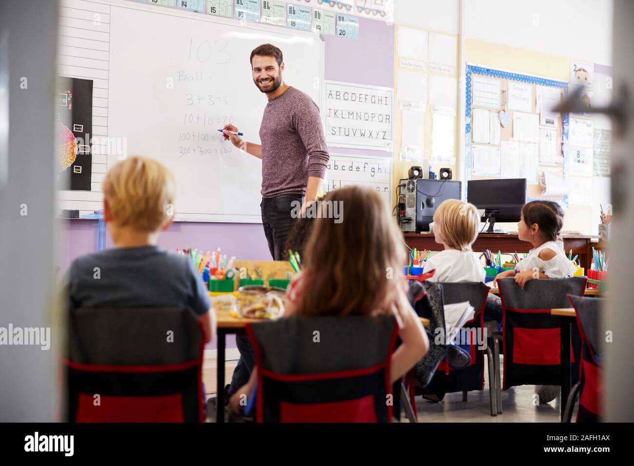 Männliche Lehrer am Whiteboard Lehre Mathe Lektion stehen Elementare Schülerinnen und Schüler In der Schule Klassenzimmer Stockfoto