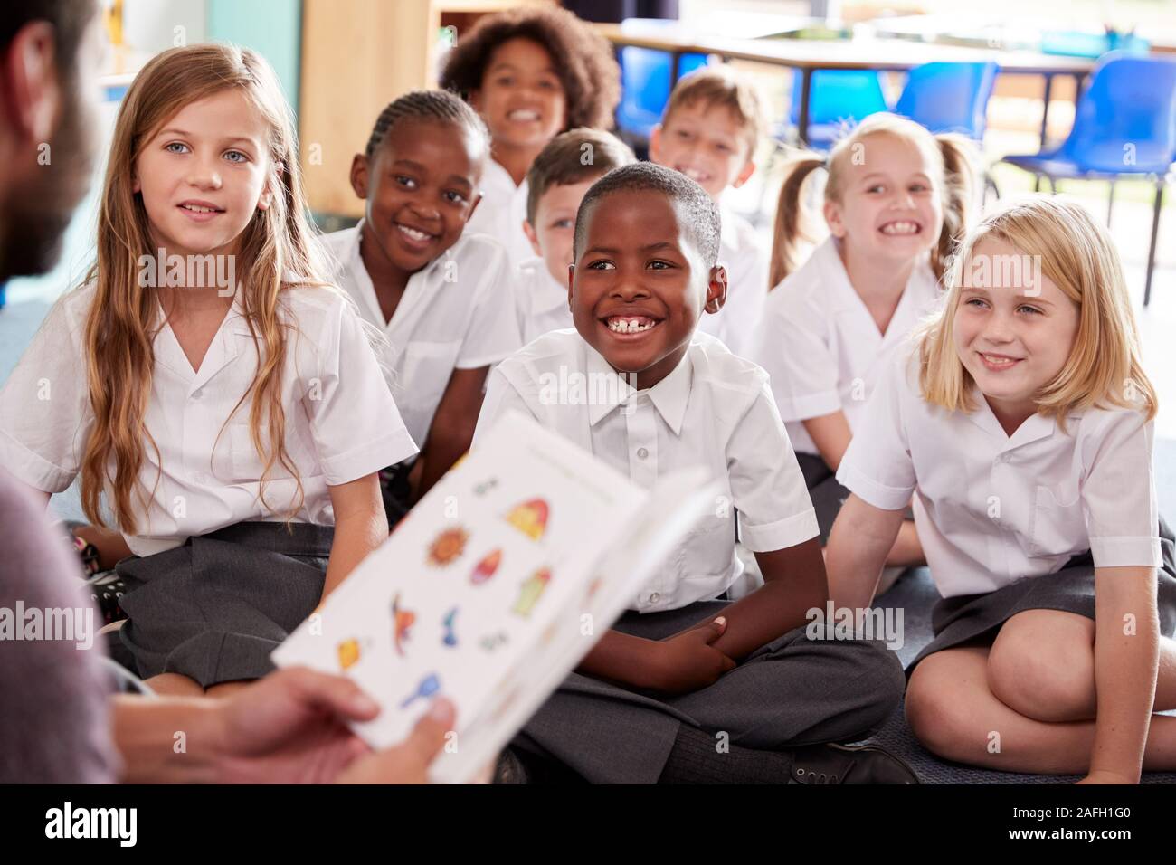 Männliche Lehrer lesen Geschichte Gruppe von elementaren Schüler Uniform tragen In der Schule Klassenzimmer Stockfoto