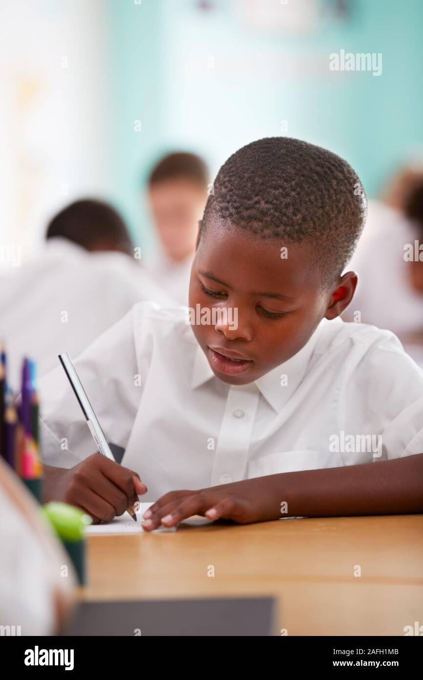 Männliche Grundschule Schüler tragen Uniform Arbeiten am Schreibtisch Stockfoto