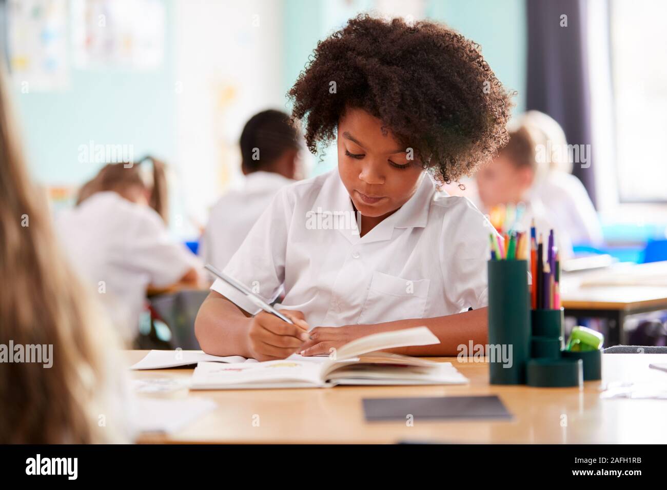 Weibliche Grundschule Schüler tragen Uniform Arbeiten am Schreibtisch Stockfoto