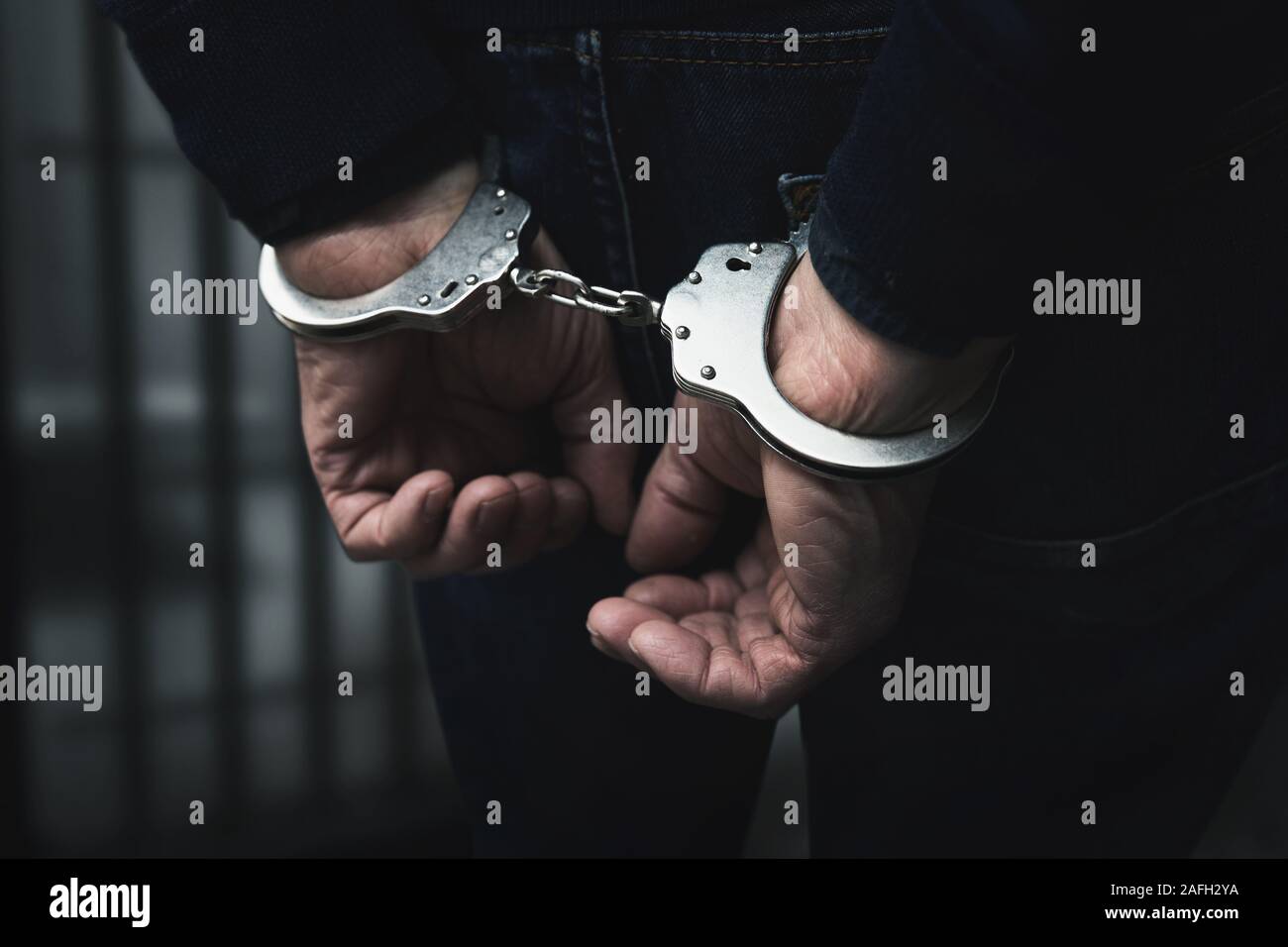 Verhaftet Mann mit gefesselten Händen hinter Gefängnis bars Stockfoto